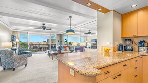 A modern kitchen with granite countertops, wooden cabinets, and a dining area with a large island. - Maui Resort Rentals: The Whaler 720/4 - 7th Floor 2BR with Gorgeous Partial Ocean and West Maui Mountain Views! (Lahaina)