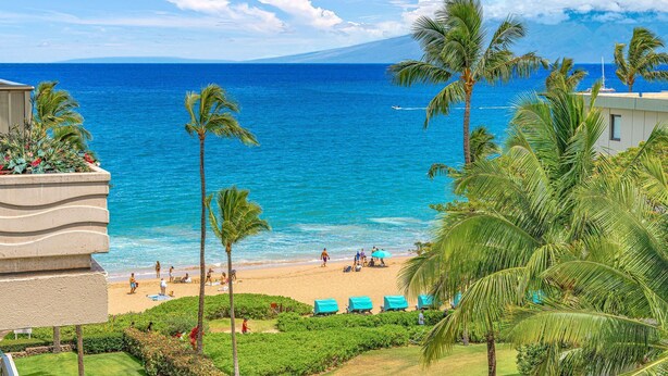 A beach view with palm trees, a sandy beach, and a clear blue ocean. - Maui Resort Rentals: The Whaler 720/4 - 7th Floor 2BR with Gorgeous Partial Ocean and West Maui Mountain Views! (Lahaina)