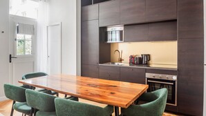 A modern kitchen with dark cabinetry, a wooden dining table, and green upholstered chairs. - Blueground | Oberkampf, washer, nr Canal (Paris)