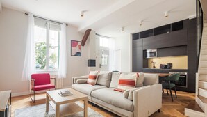 A modern living room with a sofa, a red chair, a coffee table, and a kitchen area with a stove and cabinets. - Blueground | Oberkampf, washer, nr Canal (Paris)