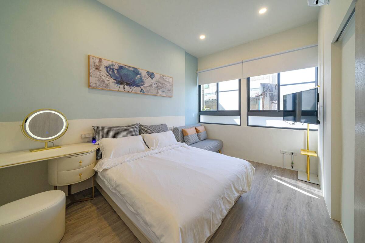 Une chambre à coucher avec un lit, une table de chevet, un miroir et une fenêtre avec des stores.