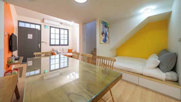 Una habitación moderna con una mesa de comedor de cristal, sillas de madera, un sofá cama, un televisor y una escalera.