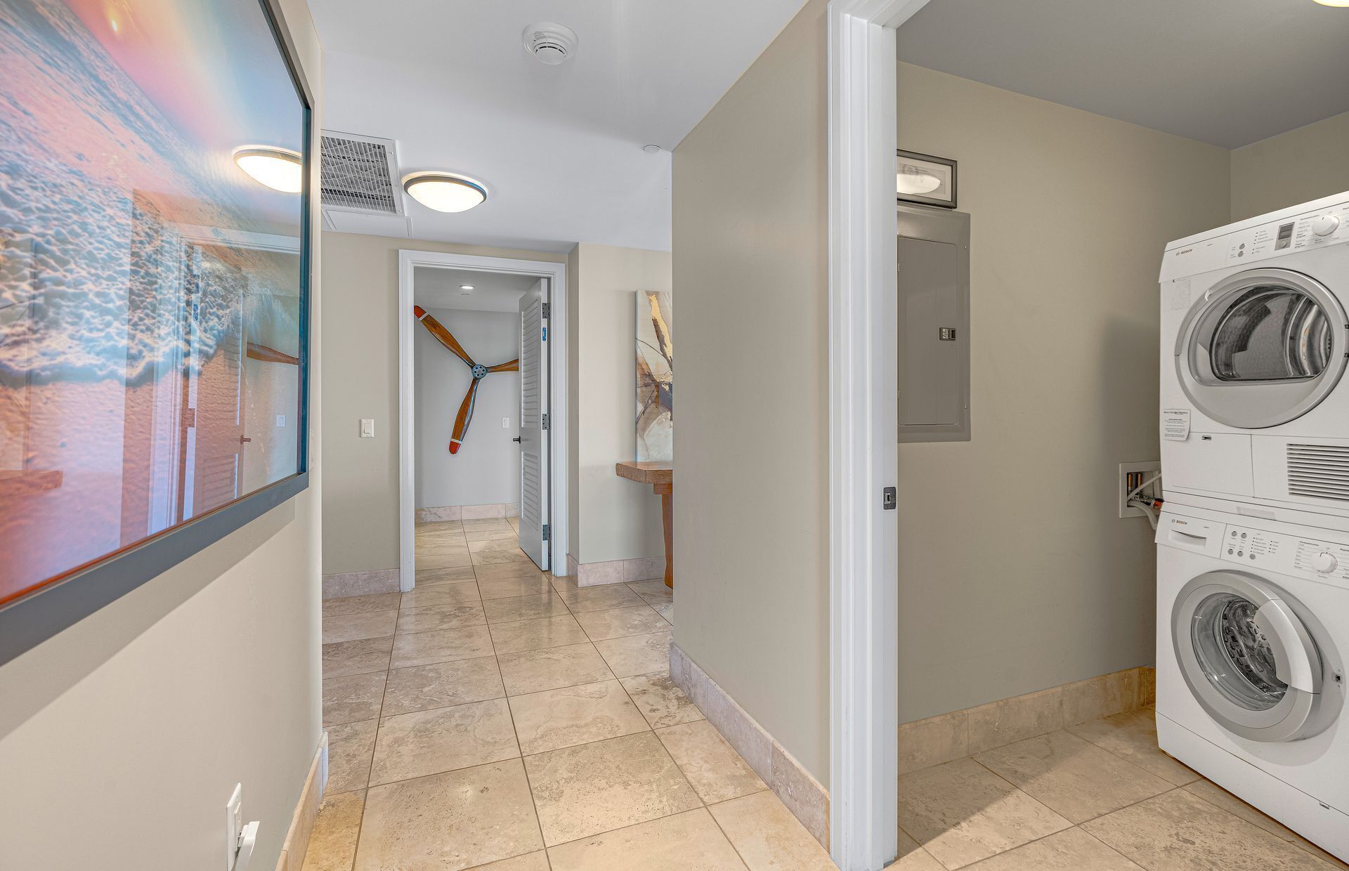 A laundry room with a front-loading washer and dryer, a ceiling fan, and a hallway leading to another room.