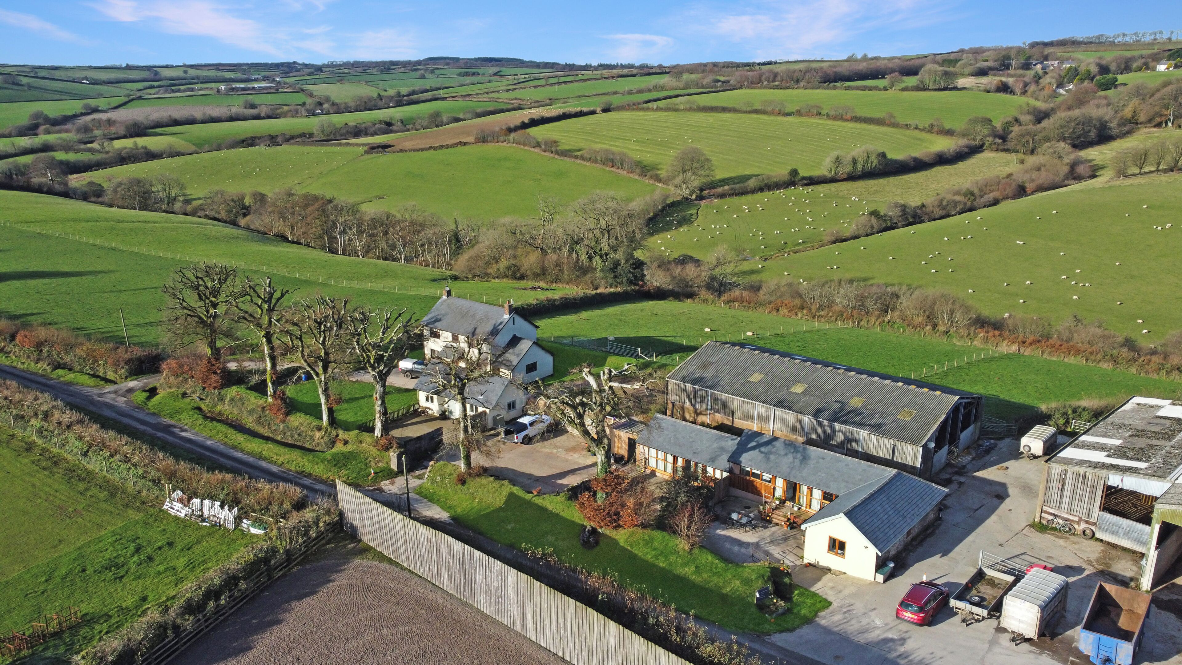 A rural property with a main house, a barn, and a fenced field with sheep.
