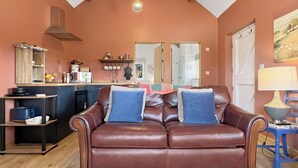 Uma sala de estar com um sofá de couro marrom, uma área de cozinha com pia e armários, e uma mesa de jantar com abajur.