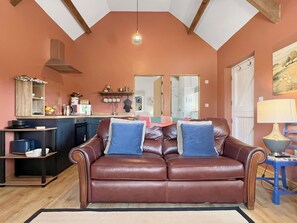 Ein Wohnzimmer mit braunem Ledersofa, einer Küchenzeile mit Spüle und Schränken sowie einem Esstisch mit Lampe.