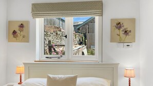 Quarto com uma janela grande, cama com duas almofadas, mesas de cabeceira com luminárias e obras de arte na parede.