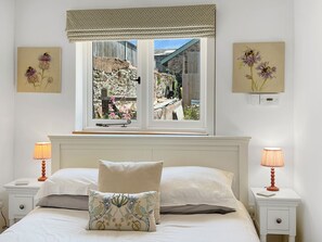 Ein Schlafzimmer mit großem Fenster, einem Bett mit zwei Kissen, Nachttischen mit Lampen und Wandbildern.