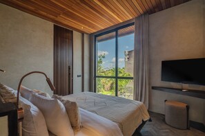 A modern bedroom with a large bed, a desk with a lamp, a TV mounted on the wall, and a sliding glass door leading to a balcony. - Sirocco Villas Pererenan (Canggu)
