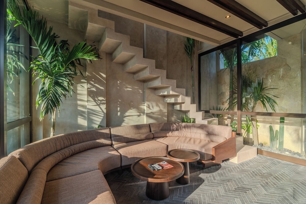 A modern living room with a curved sofa, two coffee tables, and a staircase against the wall.