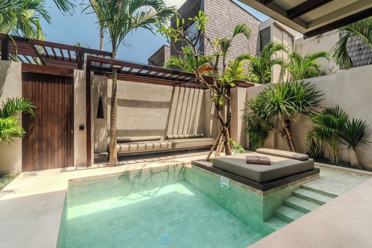 Een modern buitenzwembad met een inpandige zithoek, omringd door palmbomen en een pergola.