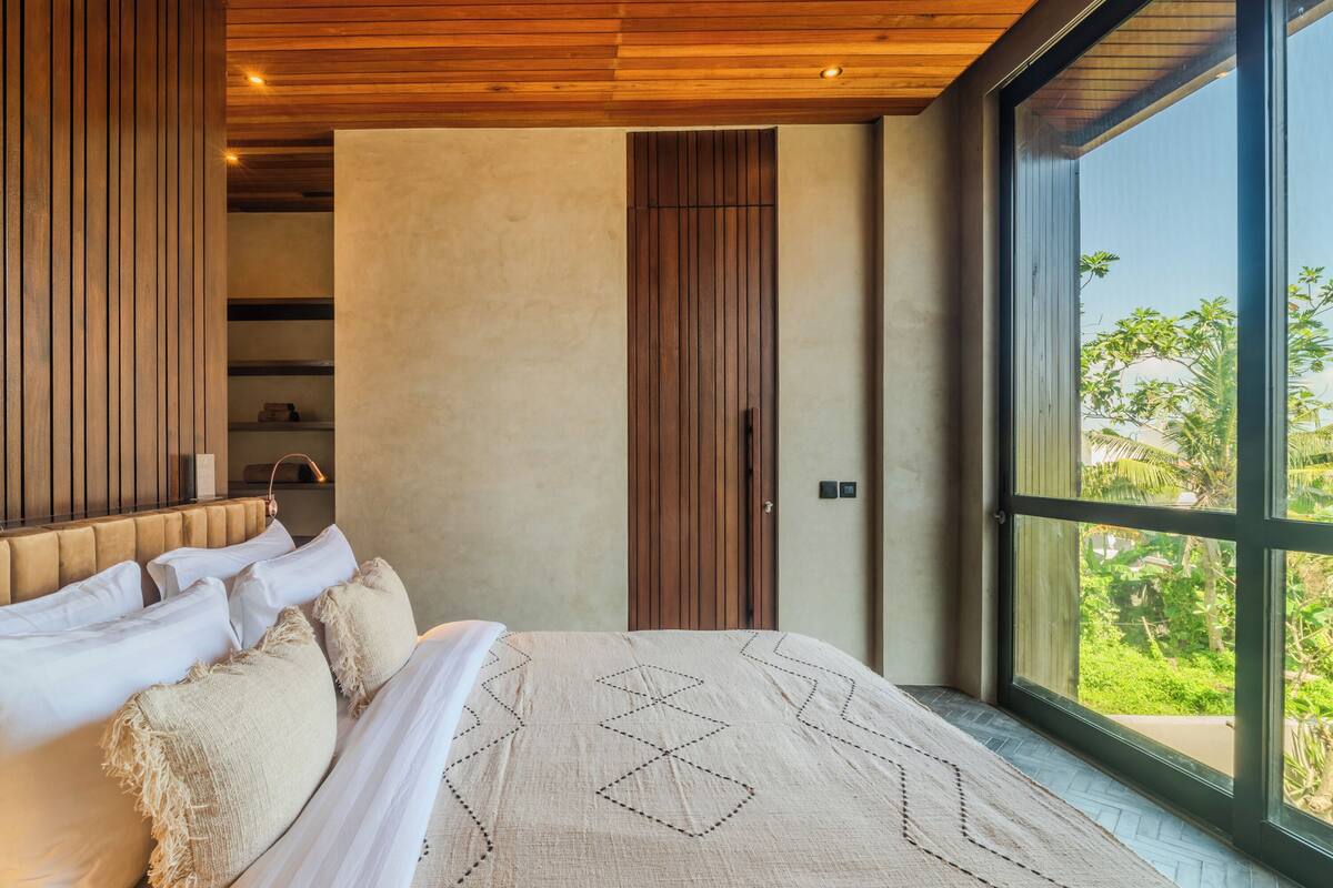 Une chambre moderne avec un grand lit, un lambris en bois et une vue sur la verdure grâce à une grande fenêtre.