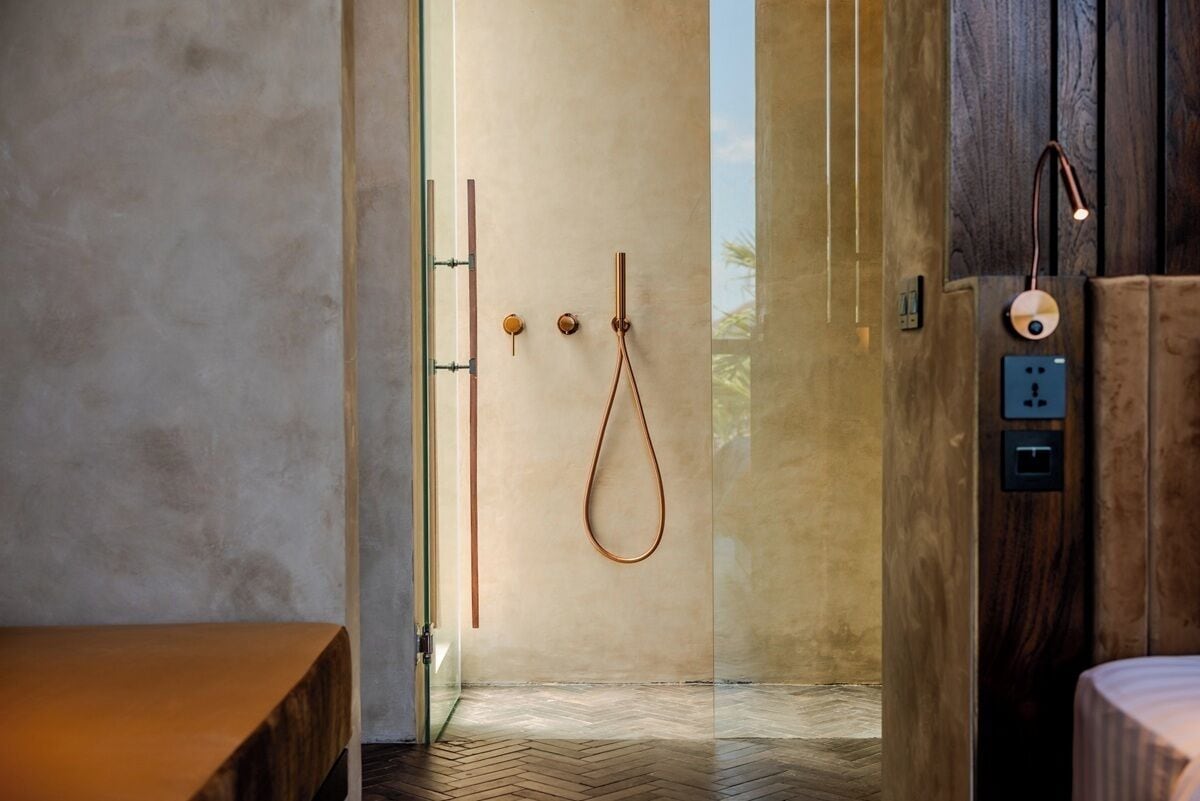 A modern bathroom with a glass shower enclosure, wooden accents, and a herringbone-patterned floor.