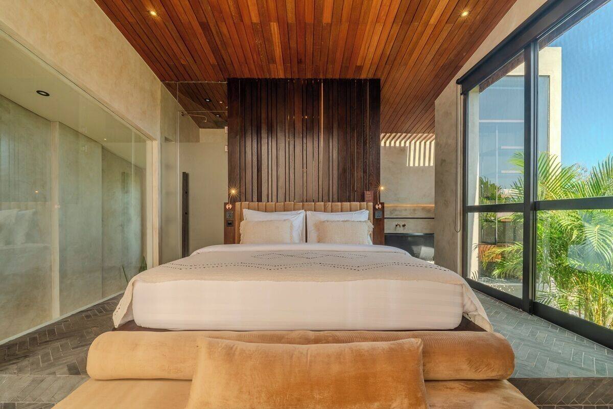 Une chambre moderne avec un grand lit, un plafond en bois et une vue sur la verdure environnante.