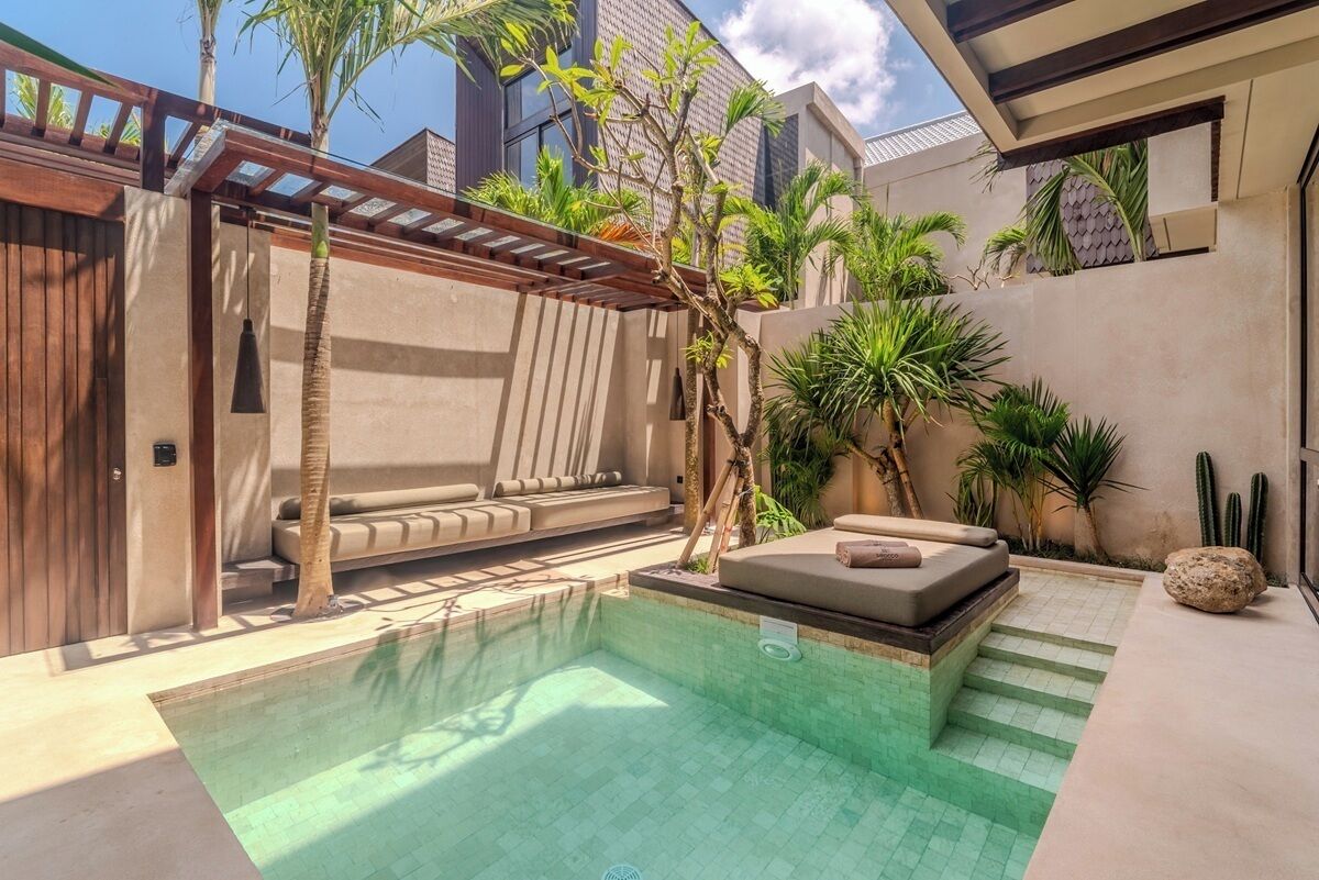 Uma área de piscina moderna ao ar livre, com espaço para sentar integrado, cercada por palmeiras e cactos.