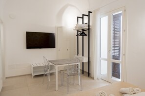 A room with a bed, a TV mounted on the wall, a table with chairs, a coat rack, and a door with blinds. - Sky D'Alcamo Rubin (Alcamo)