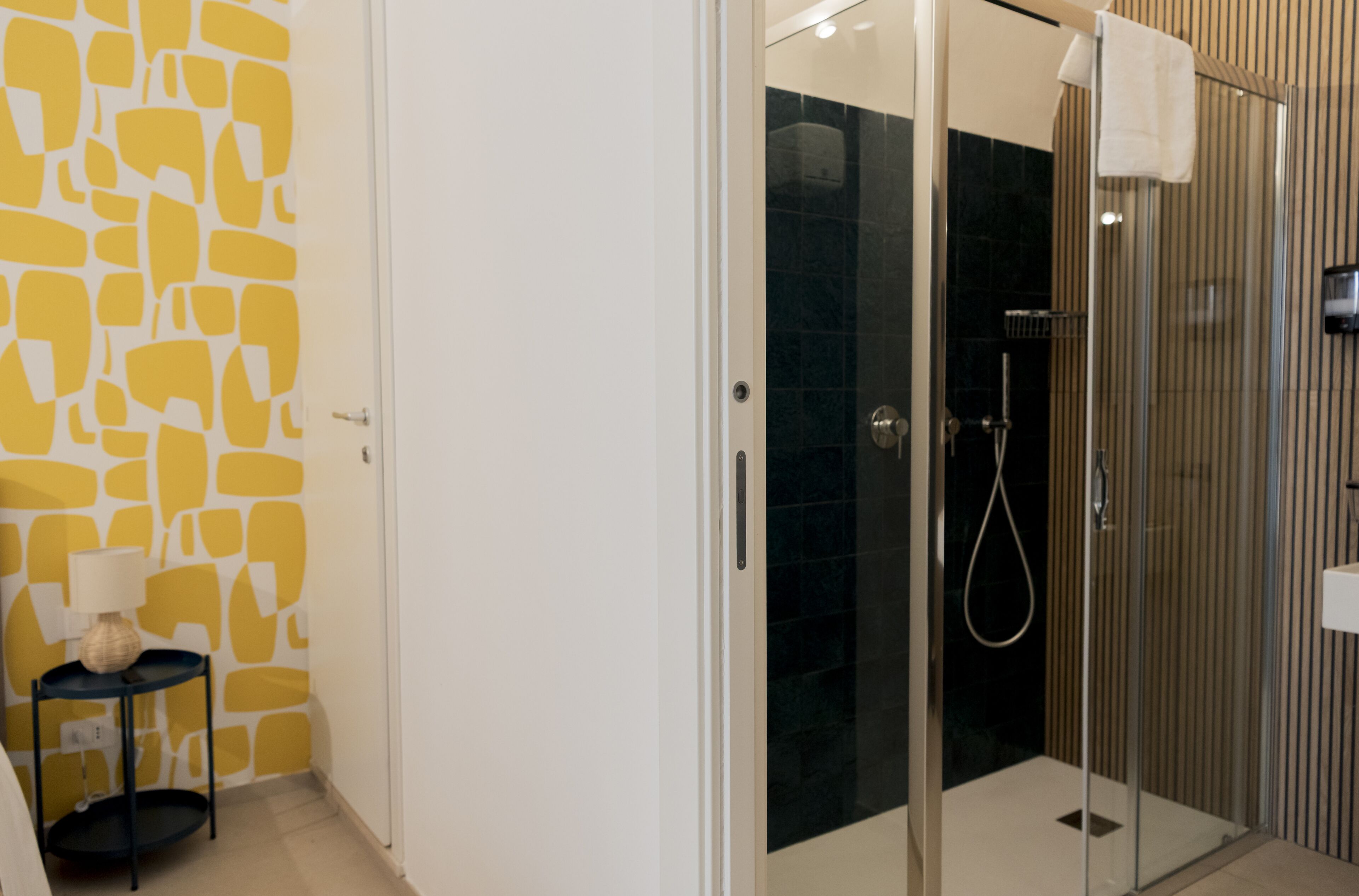 A modern bathroom with a glass shower enclosure, a white door, and a yellow patterned wall.