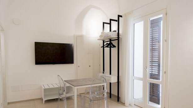 A room with a bed, a TV mounted on the wall, a table with chairs, a coat rack, and a door with blinds. - Sky D'Alcamo Diamond (Alcamo)