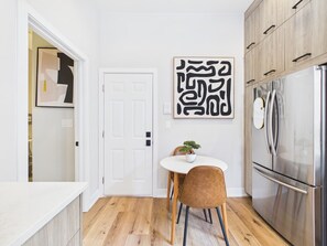 Una cocina moderna con piso de madera, un refrigerador de acero inoxidable y una mesa de comedor blanca con una silla.