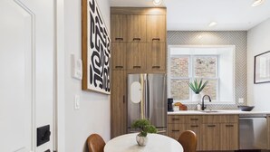 A modern kitchen with wooden cabinets, a stainless steel refrigerator, and a window with a brick wall view.