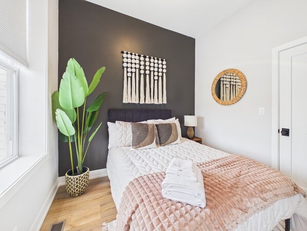 Un dormitorio con una cama, una planta en maceta, un adorno de pared y un espejo.