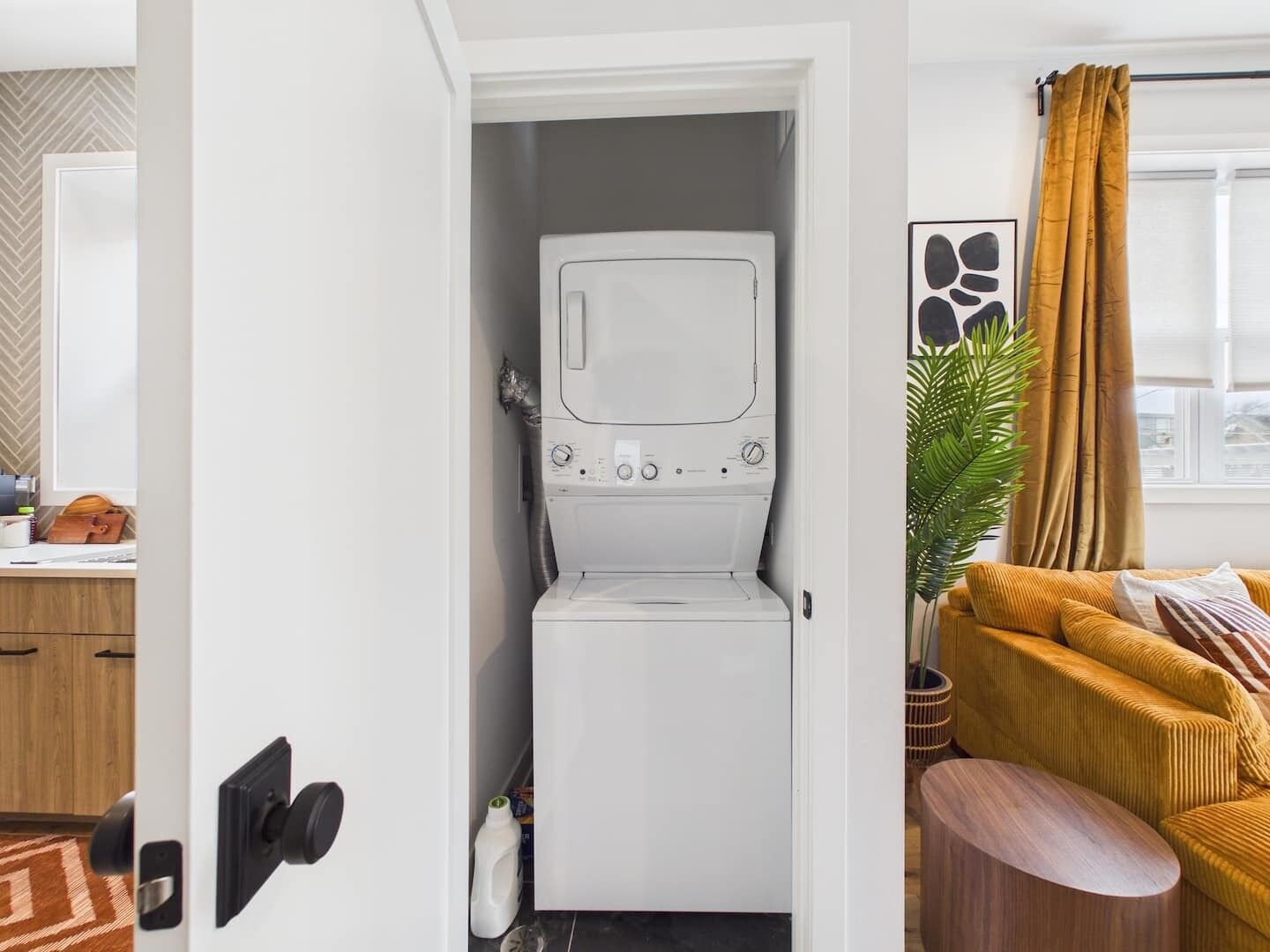 A compact laundry room with a built-in washer and dryer, a wooden cabinet, and a window with curtains.
