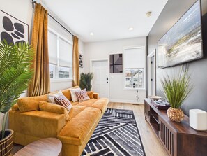 Uma sala de estar moderna com um sofá cor mostarda, um tapete preto e branco e uma pintura grande na parede.