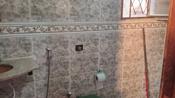 Un baño con baldosas de mármol, un inodoro con asiento verde, un cubo de basura rojo y una ventana con vistas al exterior.