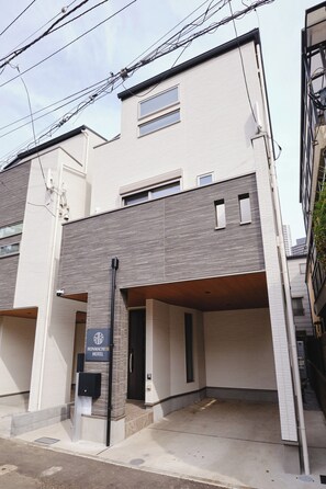 Il s'agit d'un hôtel moderne, reconnaissable à son enseigne indiquant qu'il s'agit de l'hôtel Honmachi 3B. Il se distingue par son toit plat, son espace de stationnement couvert et son design épuré et contemporain.