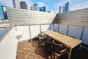 Une terrasse sur le toit, avec une table et des chaises en bois, un évier blanc et une vue sur le panorama urbain.