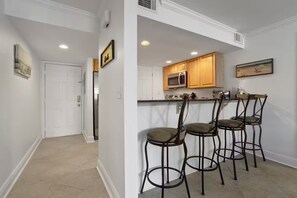 Una cocina con armarios de madera, un microondas de acero inoxidable y una zona de bar con cuatro taburetes.