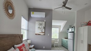 Quarto com uma cama grande, ventoinha no teto e vista para a cozinha adjacente.