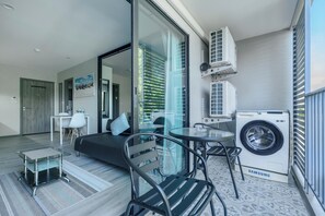 A modern apartment with a glass door leading to a balcony, a sofa, a small table, and a washing machine. - The Title Residencies Naiyang-Electricity & Water Included-F410 (Tambon Sa Khu)
