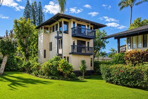 A two-story building with a balcony, surrounded by lush greenery and palm trees. - Hale Mahealani, Private Treetop Home, Ocean Views (Princeville)