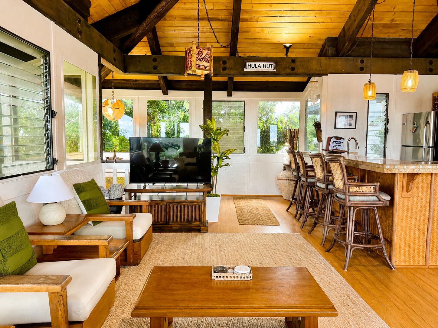 A spacious living area with a television, seating, and a kitchen area with bar stools.