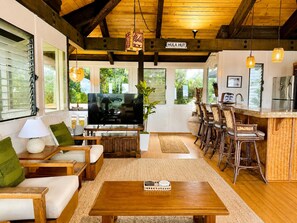 Een ruime woonkamer met een televisie, zitplaatsen en een keuken met barstoelen.