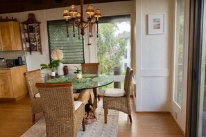 A dining area with a glass table, wicker chairs, and a hanging light fixture. - Hale Mahealani, Private Treetop Home, Ocean Views (Princeville)