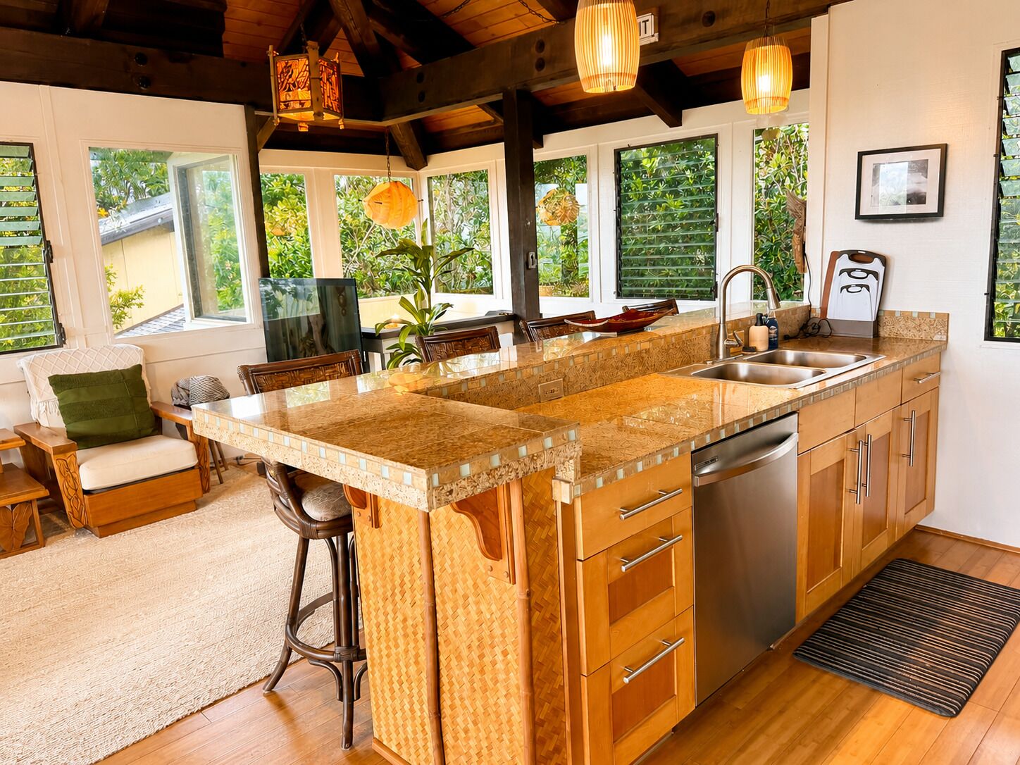 Una cocina con una isla grande, armarios de madera, un lavamanos de acero inoxidable y un comedor con sofá y sillas.