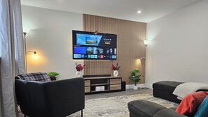 A modern living room with a flat-screen TV mounted on the wall, a sofa, a coffee table, and a decorative plant. - Elegant 3-bedroom Home Away From Home, Luxury Styled (St. John's)