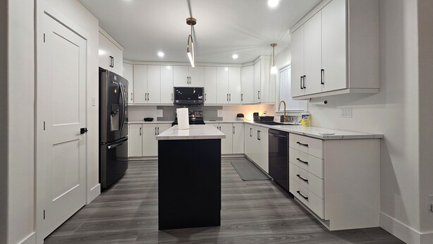 A modern kitchen with white cabinetry, a black refrigerator, and a central island. - Elegant 3-bedroom Home Away From Home, Luxury Styled (St. John's)