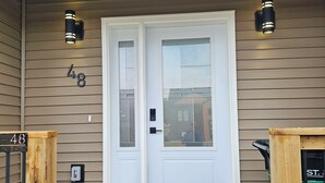 A front door with a number "48" on the wall, a black doormat, and two wall-mounted lights. - Elegant 3-bedroom Home Away From Home, Luxury Styled (St. John's)