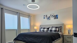 A bedroom with a bed, bedside tables, a ceiling light, and artwork on the wall. - Elegant 3-bedroom Home Away From Home, Luxury Styled (St. John's)