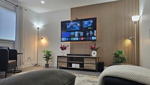 A modern living room with a flat-screen TV mounted on a wooden wall, a sofa, a coffee table, and a potted plant. - Elegant 3-bedroom Home Away From Home, Luxury Styled (St. John's)