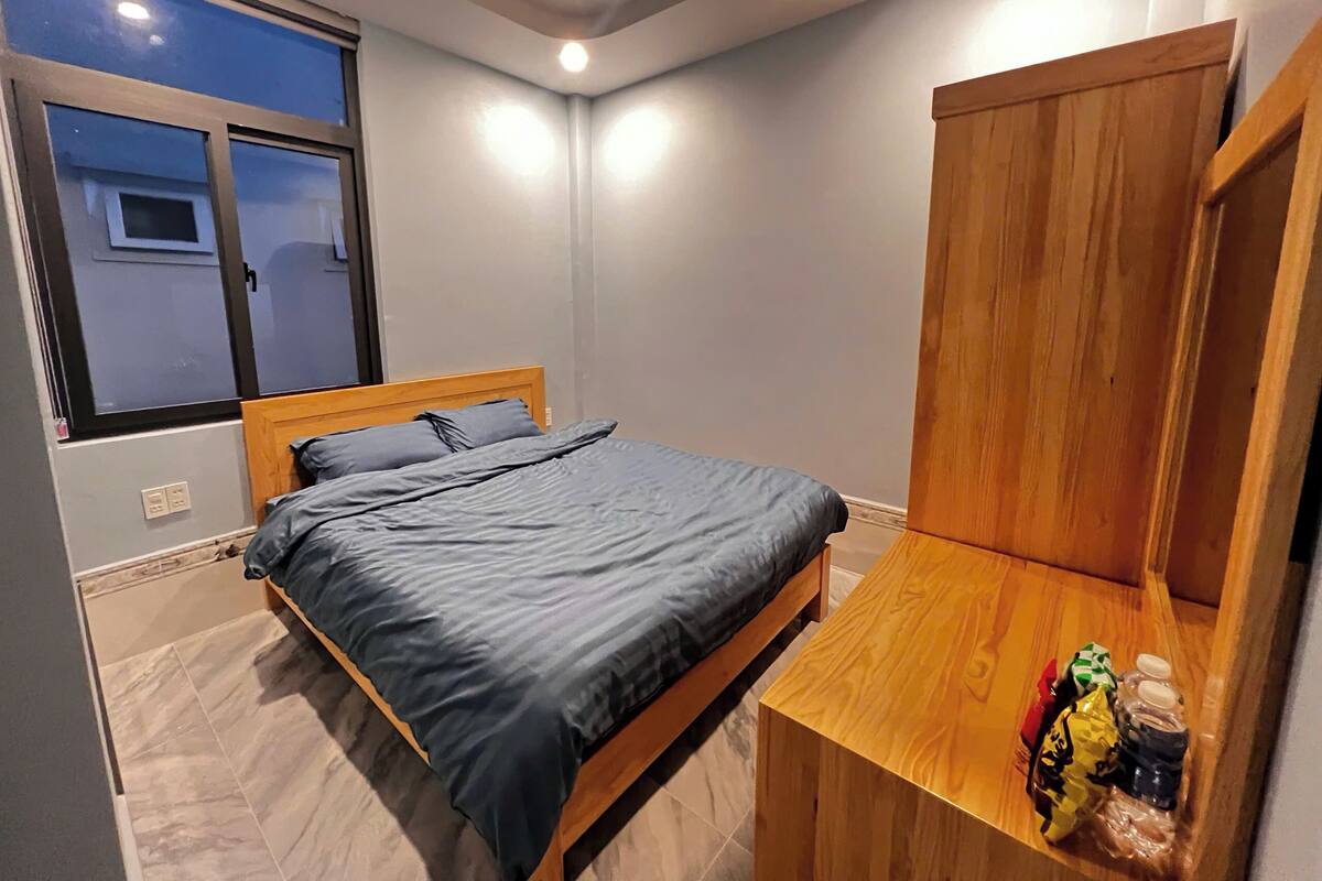 Un dormitorio con cama, un armario de madera, una mesita y una ventana.