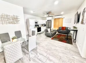 A modern living room with a grey sofa, a dining area with a table and chairs, and a kitchen area with white cabinets and appliances. - Uniktrend Campo Rd Home by SD Stay (Spring Valley)