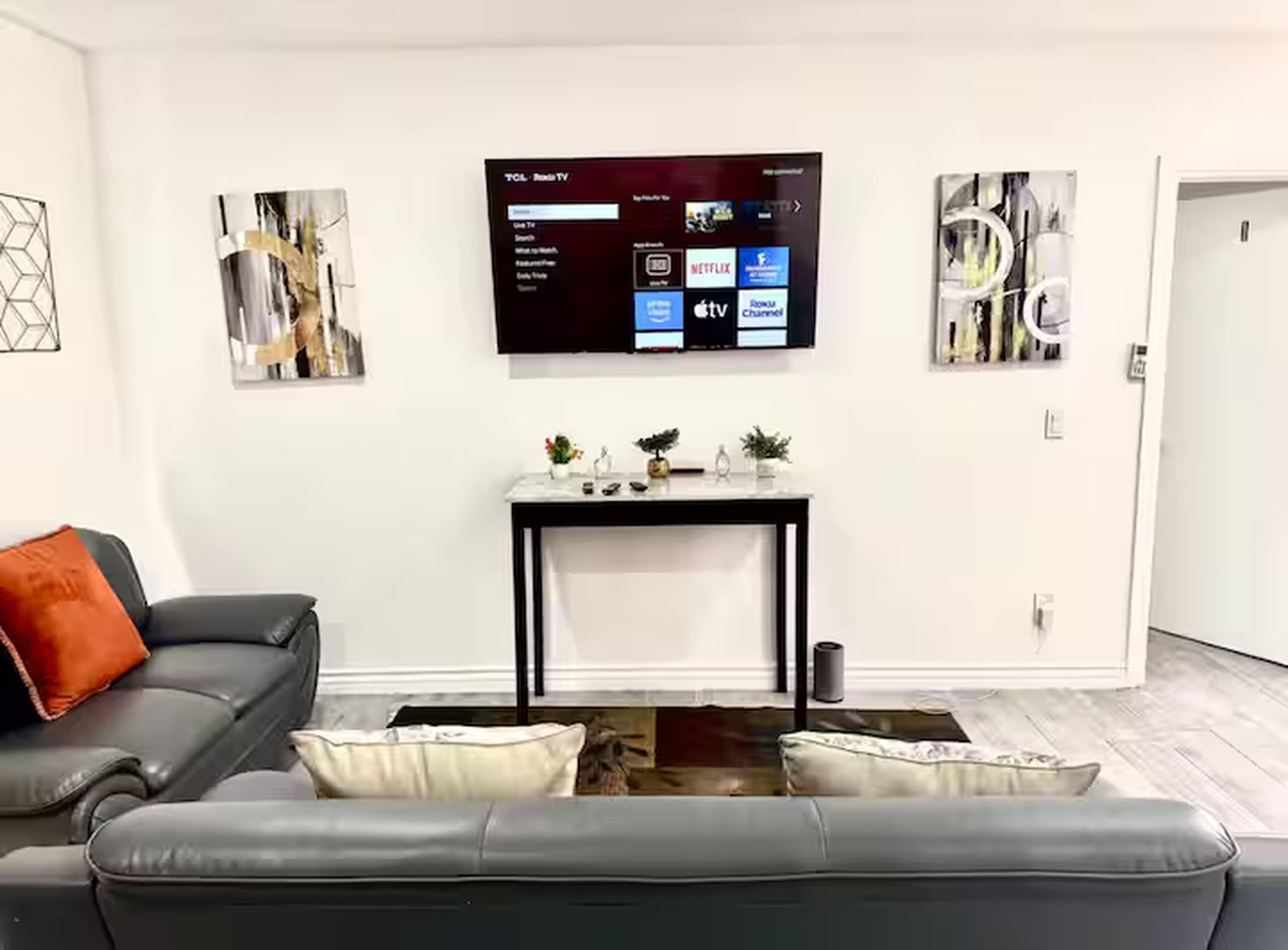 A modern living room with a black leather sofa, a coffee table, and a flat-screen TV mounted on the wall displaying streaming services.