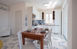 Un comedor con mesa de madera y sillas blancas, una cocina con azulejos azul y blanco, y un ventanal con vistas.