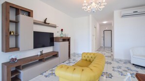 Una sala de estar con un sofá amarillo, un televisor de pantalla plana, estanterías de madera y una araña.