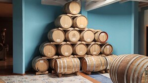 Weinhähne aus Holz sind zu einer Pyramide aufgestapelt, vor einer blauen Wand in einem Raum mit Fliesenboden.