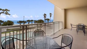 Un balcon avec une table et des chaises, donnant sur une piscine et l’océan.